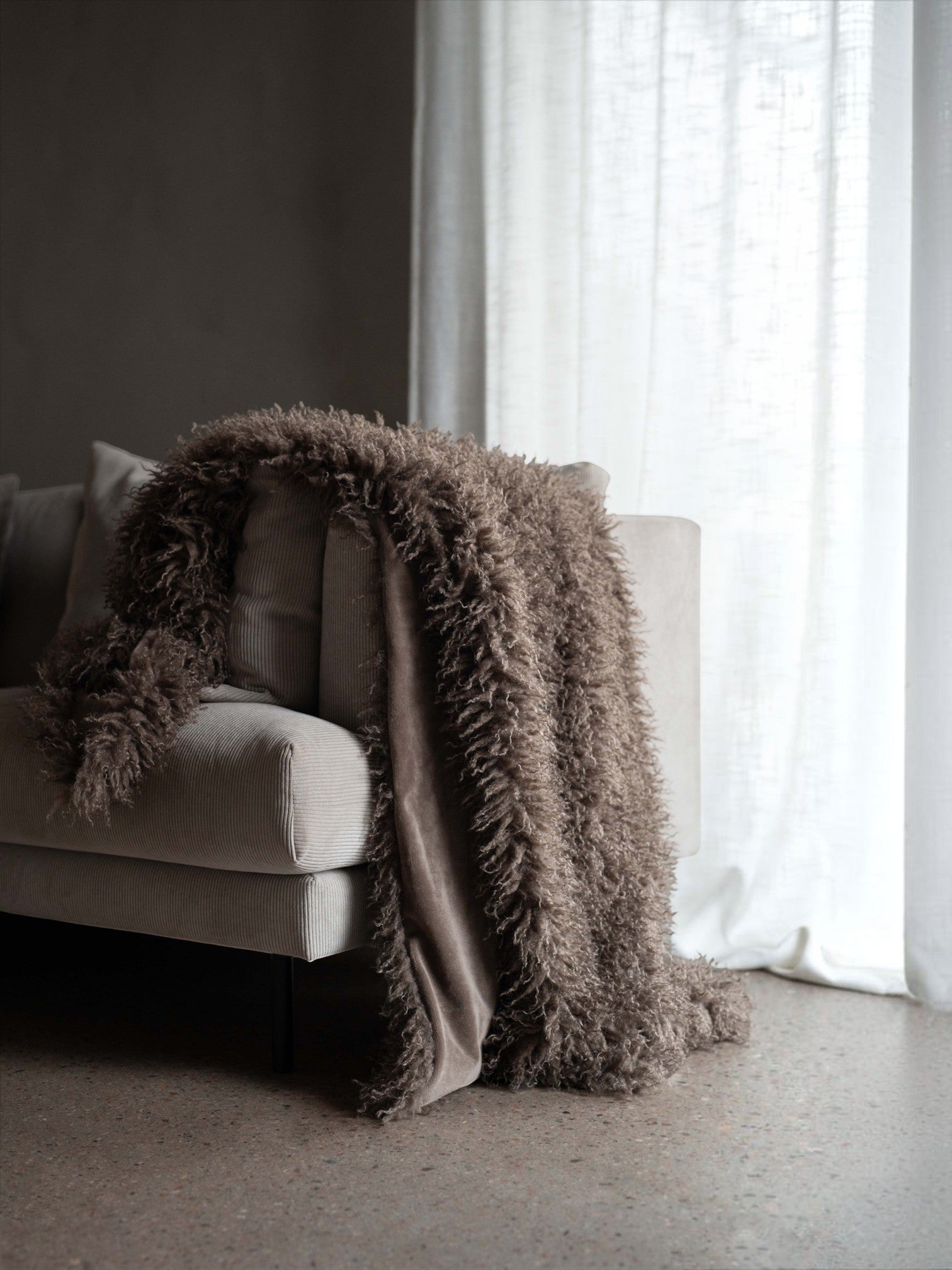 Lyckåsen brown faux fur throw blanket with curly Tibetan sheepskin texture draped over a beige corduroy sofa