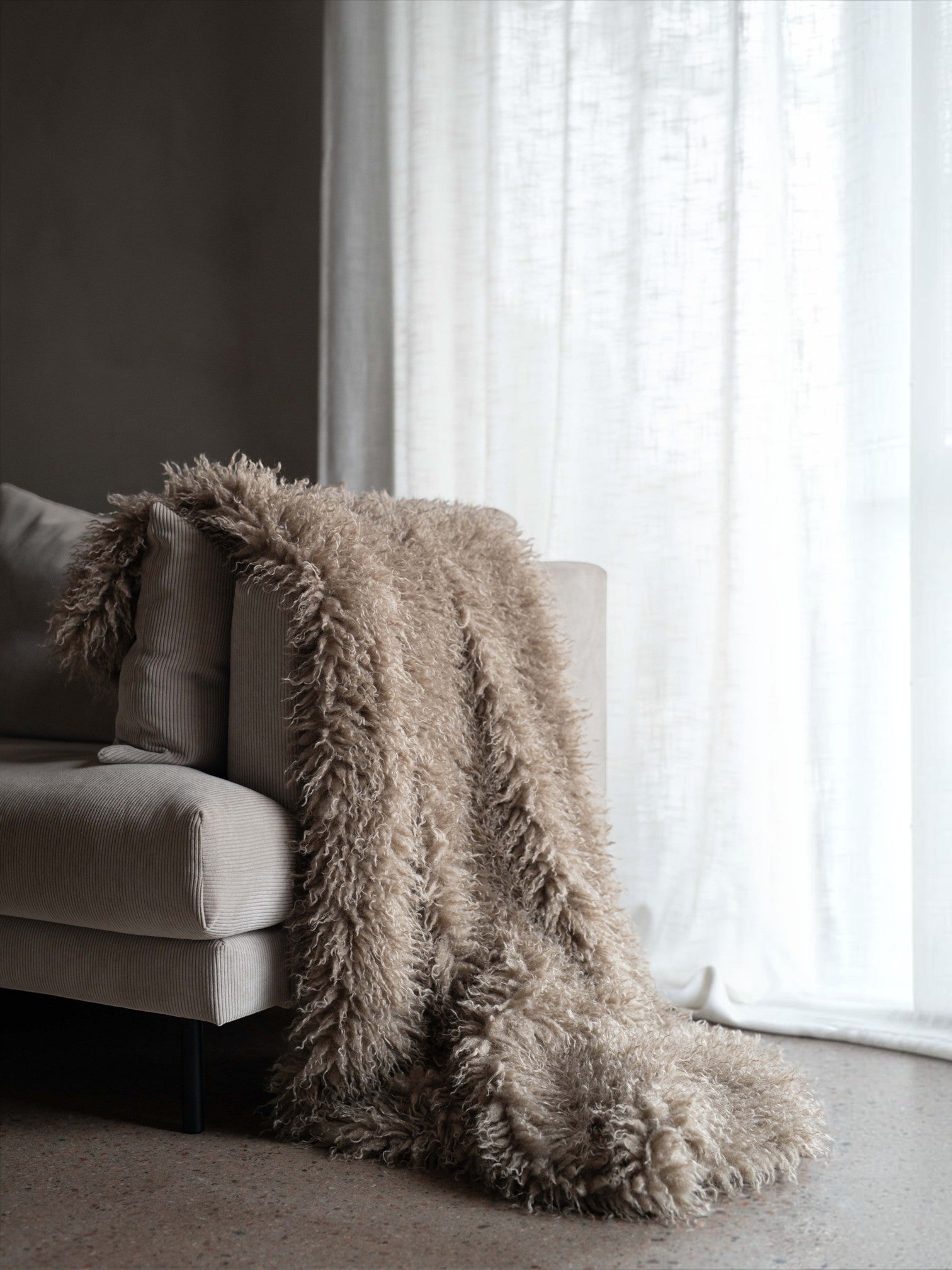 Lyckåsen Curly throw blanket in sand faux fur with a Tibetan sheepskin look draped over a beige corduroy sofa.