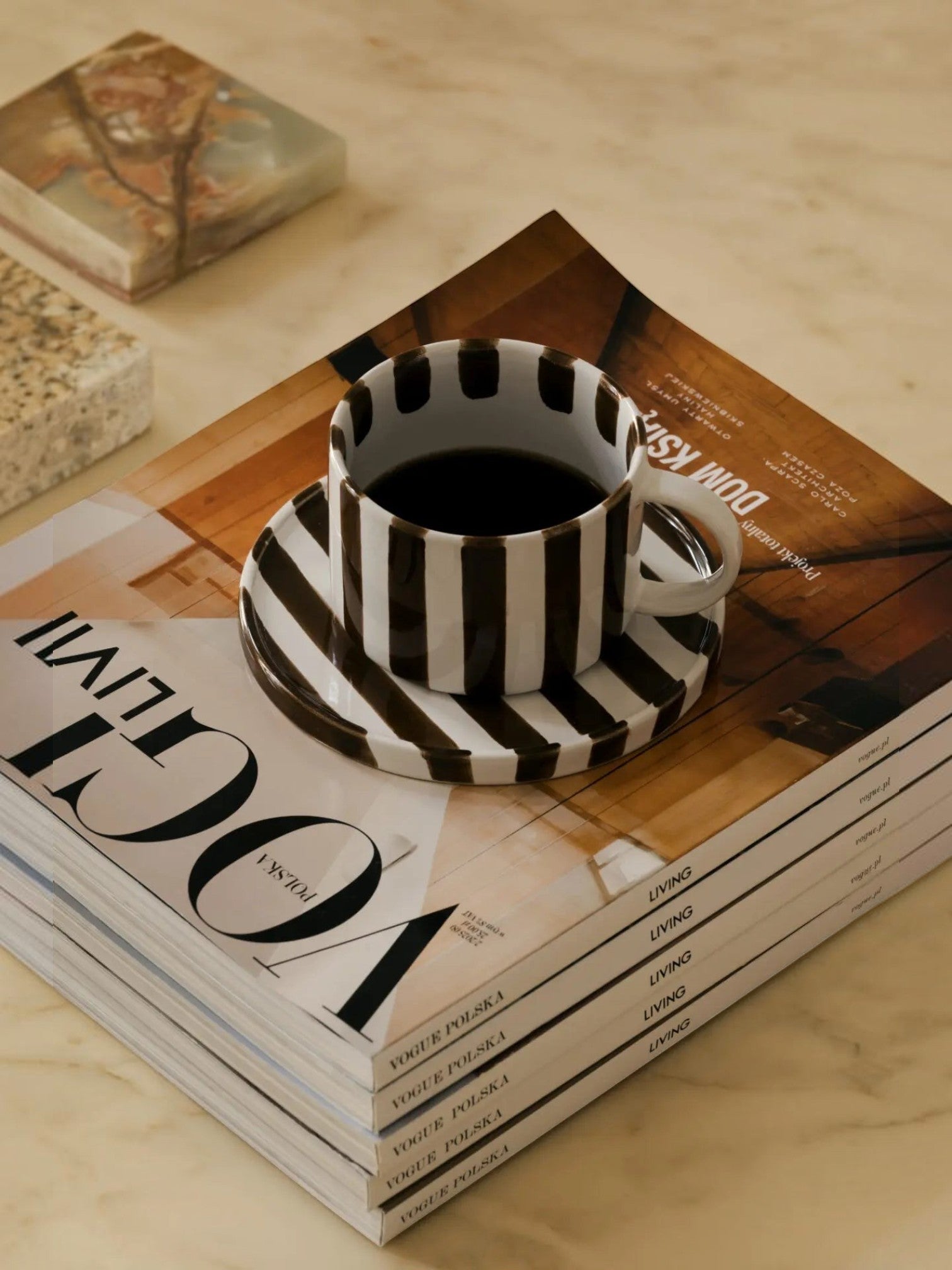 Lyckåsen Monica hand-painted brown and white striped ceramic coffee cup and saucer resting on a stack of magazines.