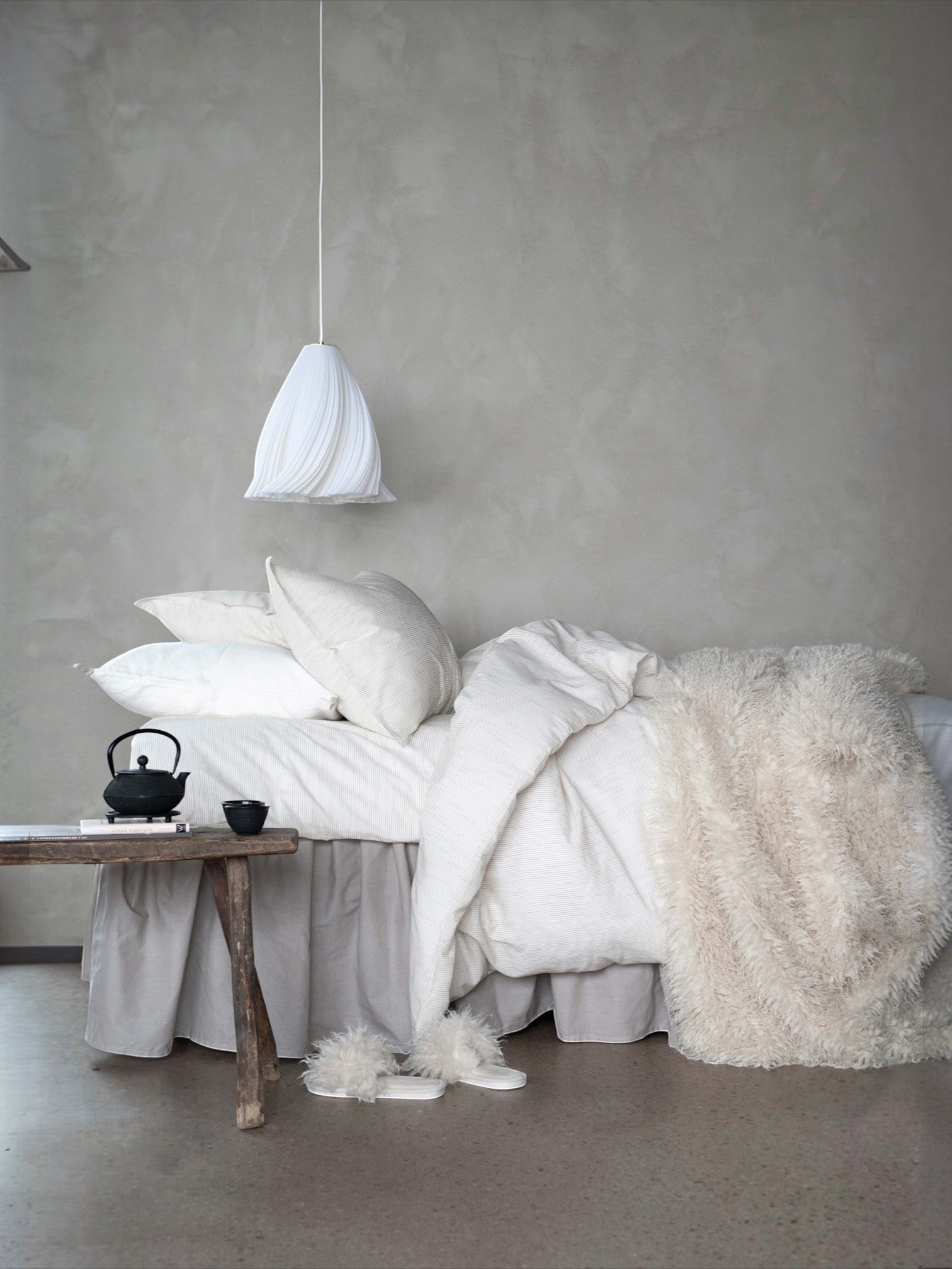 Lyckåsen off-white faux fur throw blanket with curly texture draped over a bed in a cozy minimalist bedroom.