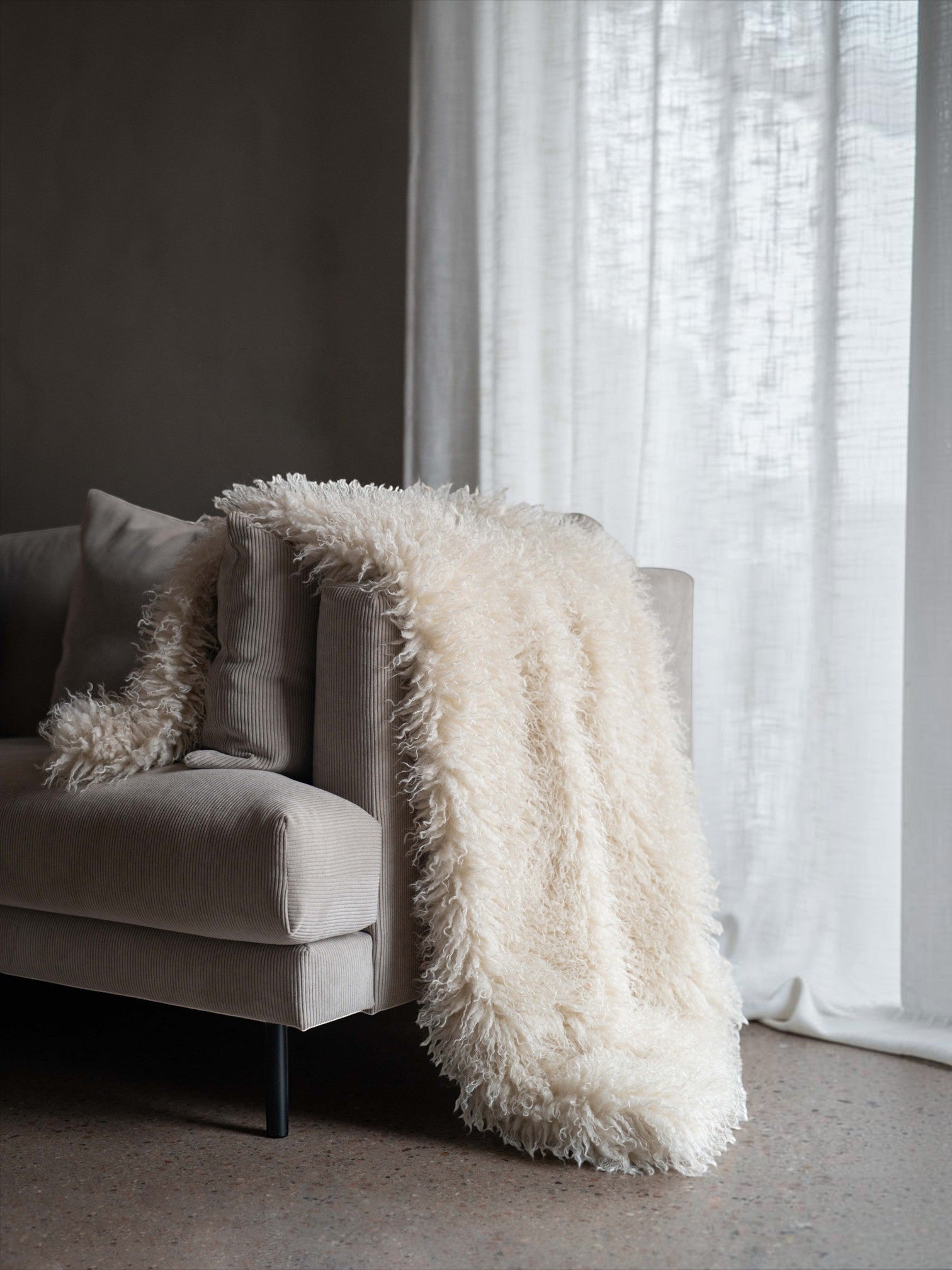 Lyckåsen off-white faux sheepskin throw blanket with curly texture draped over a modern beige corduroy sofa