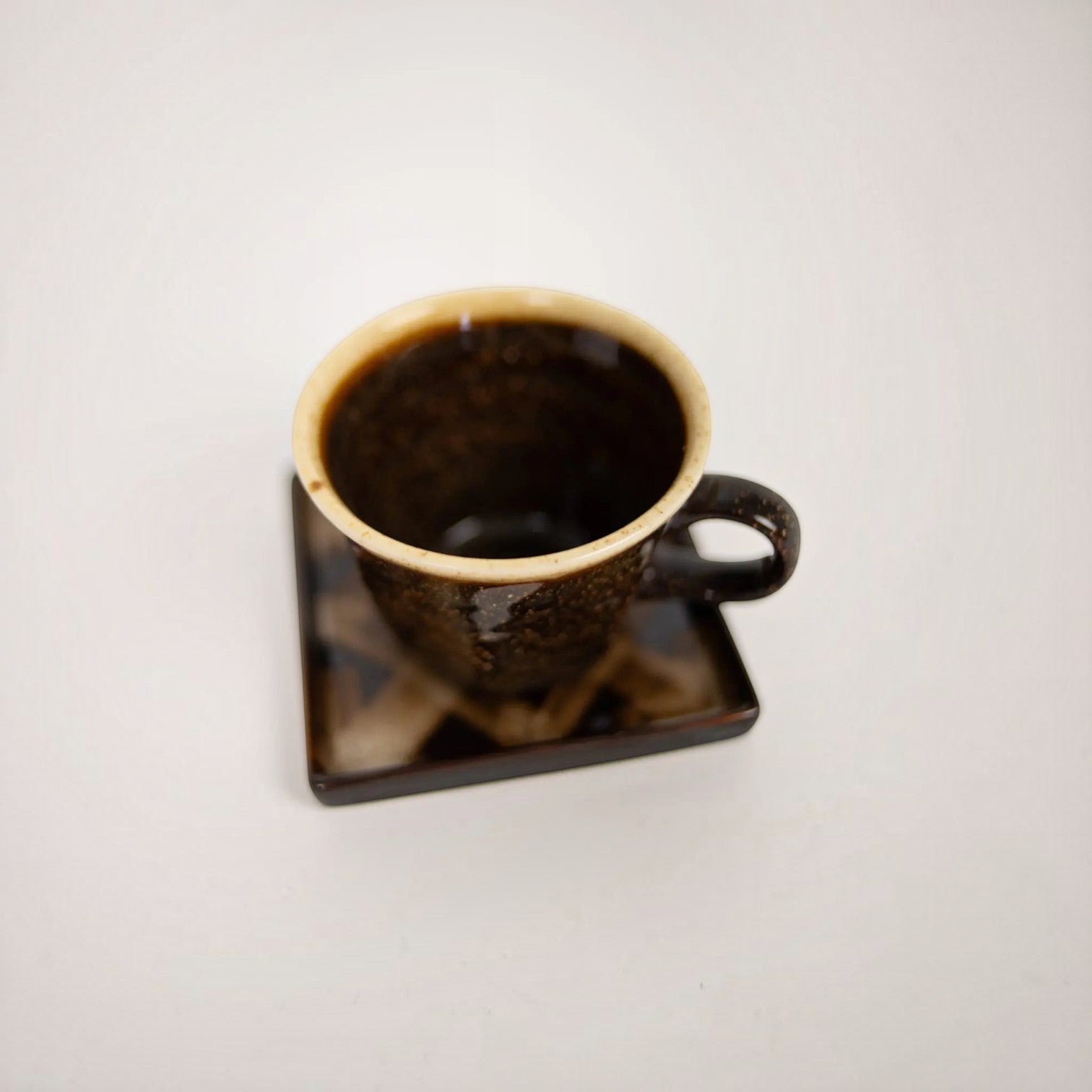 Lyckåsen stoneware coffee cup and square saucer set with dark rustic glaze and a contrasting light rim