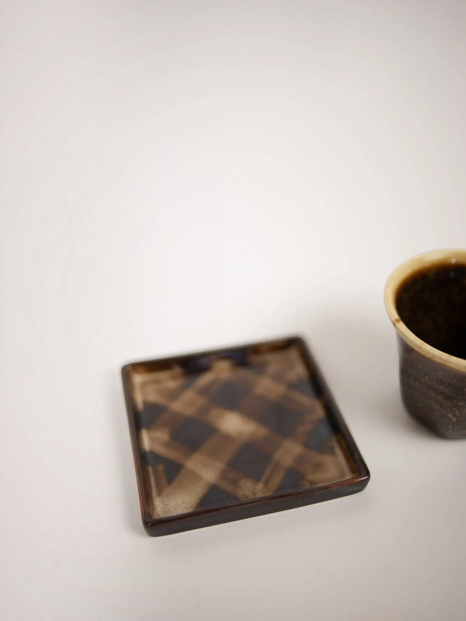 Lyckåsen stoneware cup and square checkered saucer set with dark rustic glaze and light rim detail