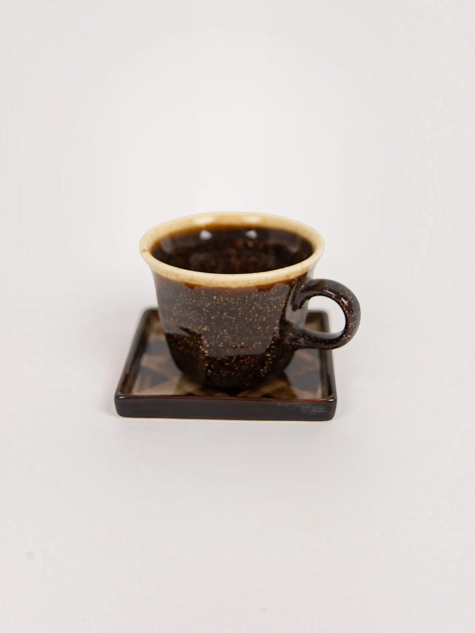 Lyckåsen stoneware cup and square saucer set with dark speckled glaze and a contrasting light rim.